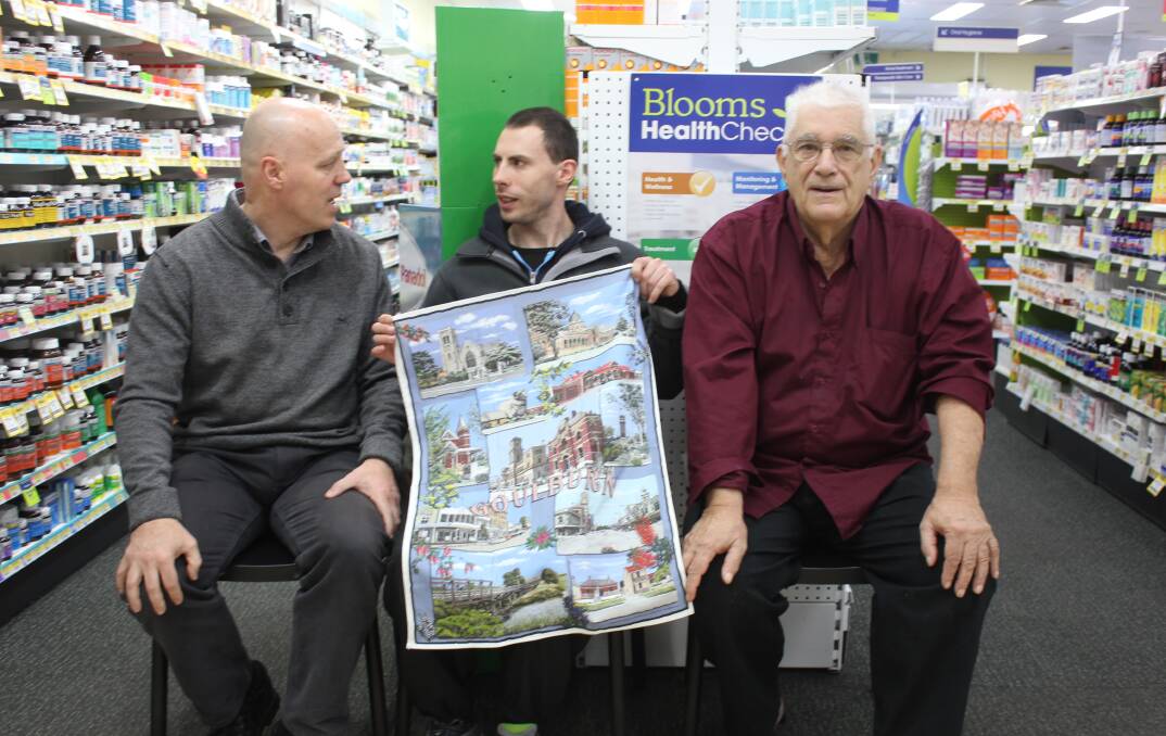 COLOURFUL: Peter and Matthew Blematl and artost Jean Pierre Favre in Blooms Chemist on Wednesday with the new Goulburn tea-towel. 