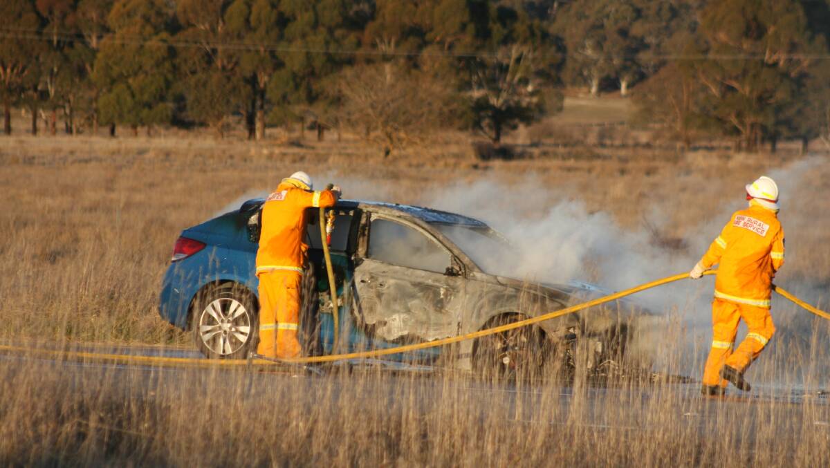 CAR FIRE: Officers from the NSW Rural Fire Service extinguish the car on fire near Collector on Saturday afternoon. 