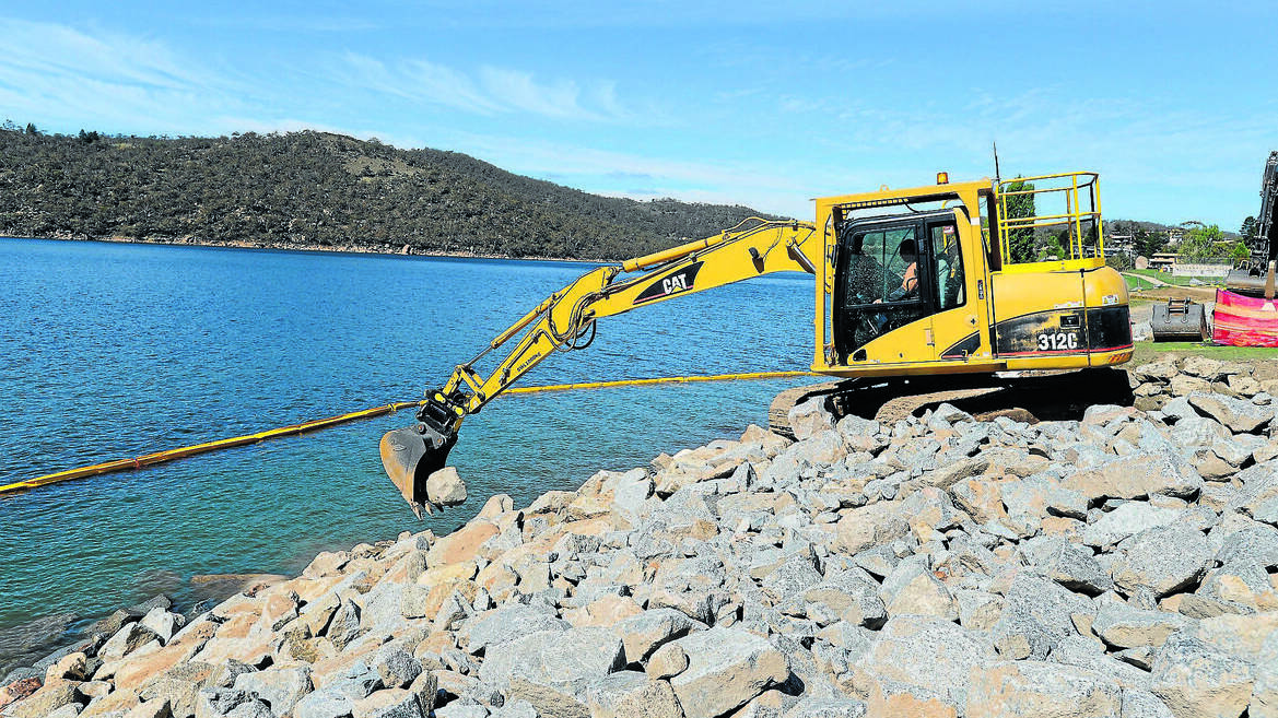JINDABYNE: Simon Rees deposits the rock into position on the lake foreshore. Photo: Steve Cuff, Summit Sun.