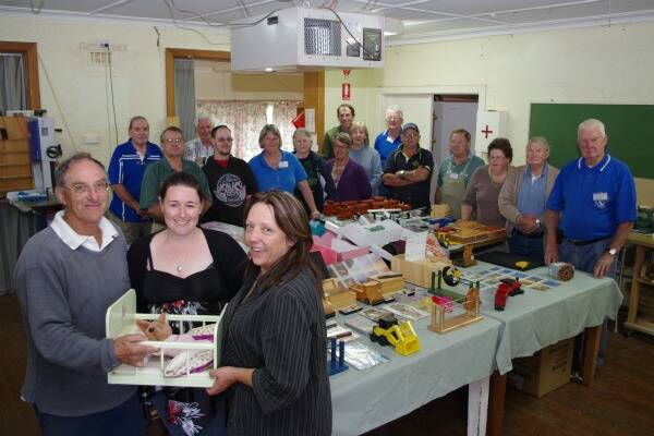 GENEROSITY: Goulburn Region Woodworkers president Jack Treweek presents a toy baby’s cradle and doll to Anglicare Goulburn representatives Toni Rae and Amanda Greening, watched by members of the club surrounding the table of hand crafted wooden toys and other items on Wednesday evening.