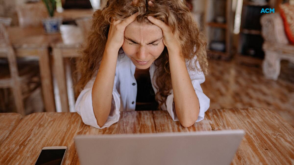 Woman sits at her laptop, stressed. Picture via Canva