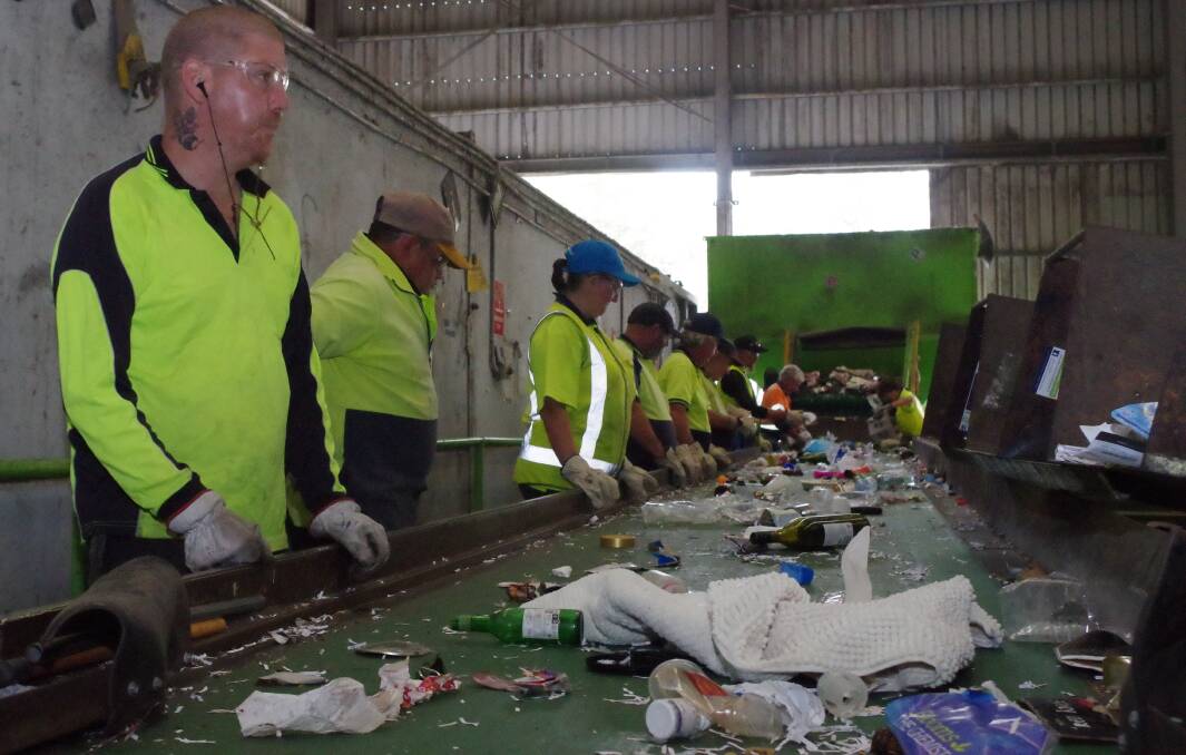 CONTAMINATION: Endeavour Industries workers sorting recyclable material from the rubbish (in the foreground) including a dirty nappy, unusable plastics, a green bottle and a cot cover. Photo: Darryl Fernance