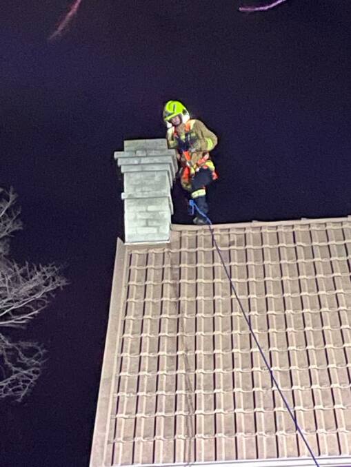 A firefighter prepares to dangle a rope in the chimney for the possum to free itself.