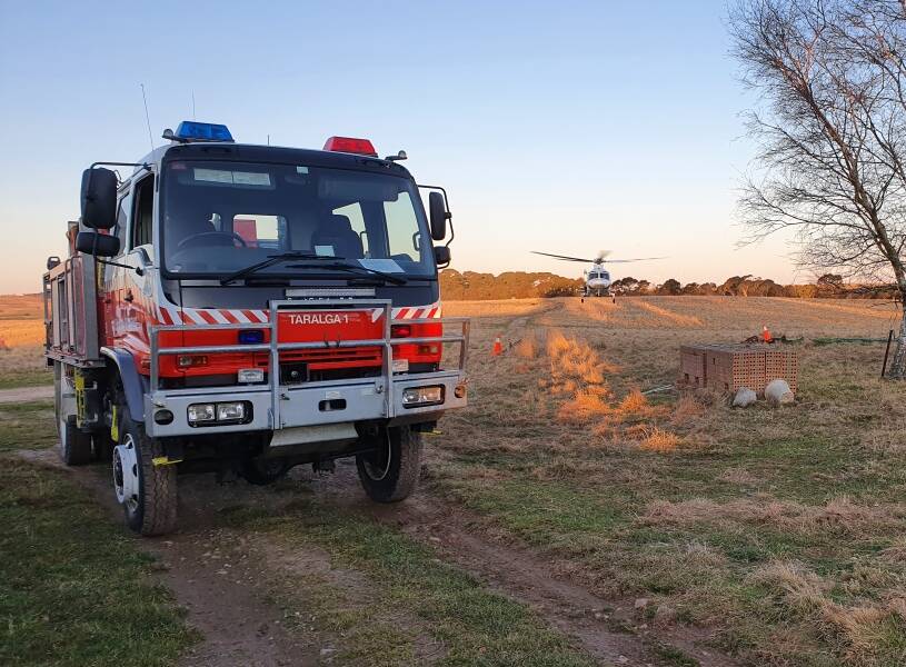 Taralga RFS at the scene of an internal house fire near the town on Friday. At rear, a Toll helicopter prepares to air-lift an injured man to hospital. Photo: Taralga RFS.