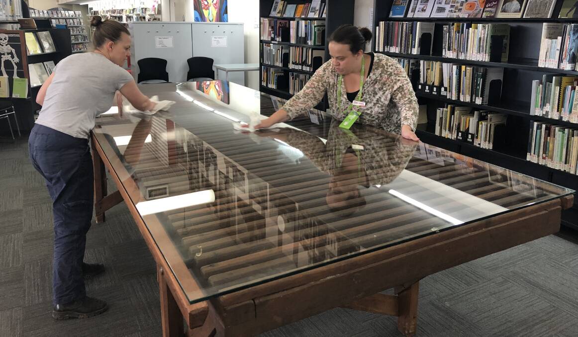 CHARACTER: Library assistants Amber Barber and Madeline Young cleaning the former wool-classing table after its installation into the Goulburn Mulwaree Library. Photo supplied.  