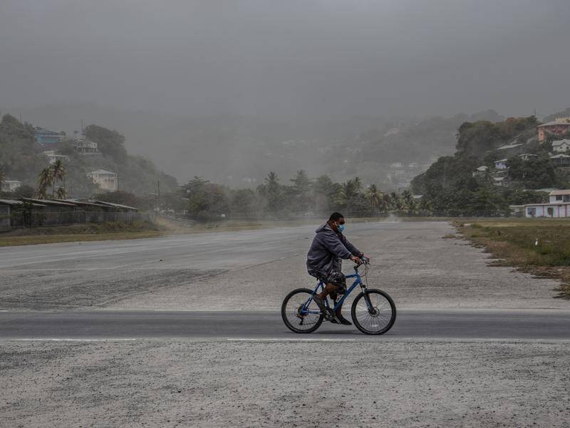A man rides his bicycle past fields covered with ash a day after the La Soufriere volcano erupted.