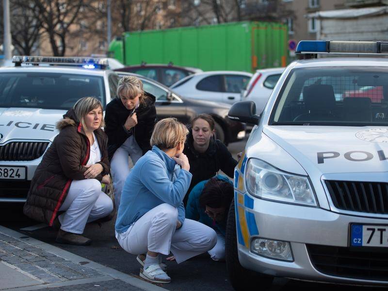 Hospital staff hide behind police vehicles near the scene of the shooting at a hospital in Ostrava.