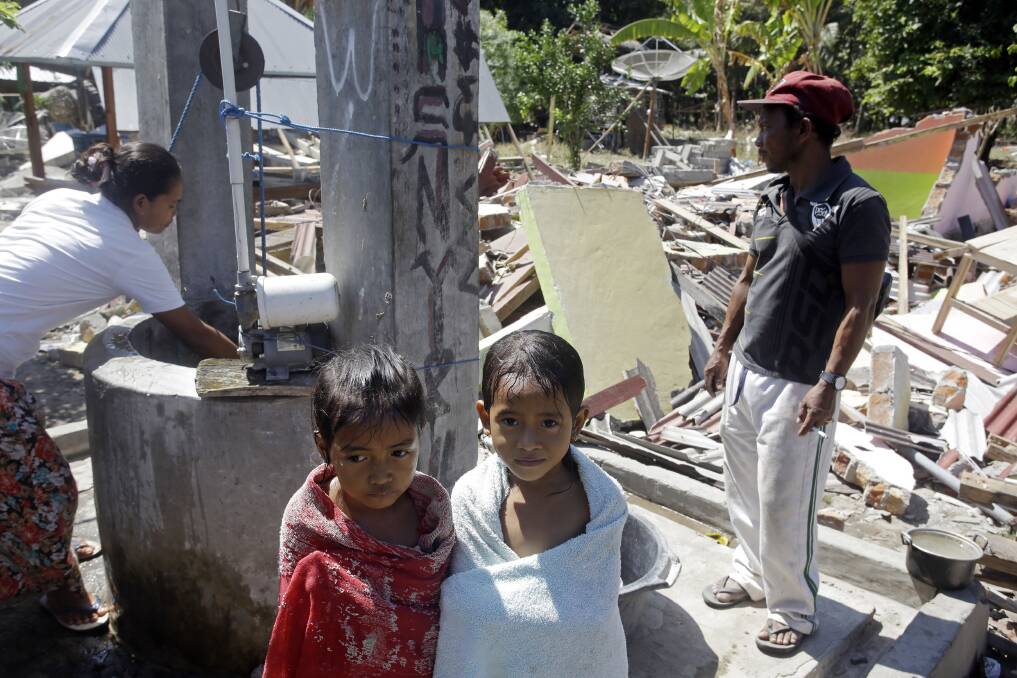 Children cover themselves with towels after a bath near their home destroyed by last week's Indonesian earthquake, Sunday, Aug. 12, 2018. (AP Photo/Firdia)
