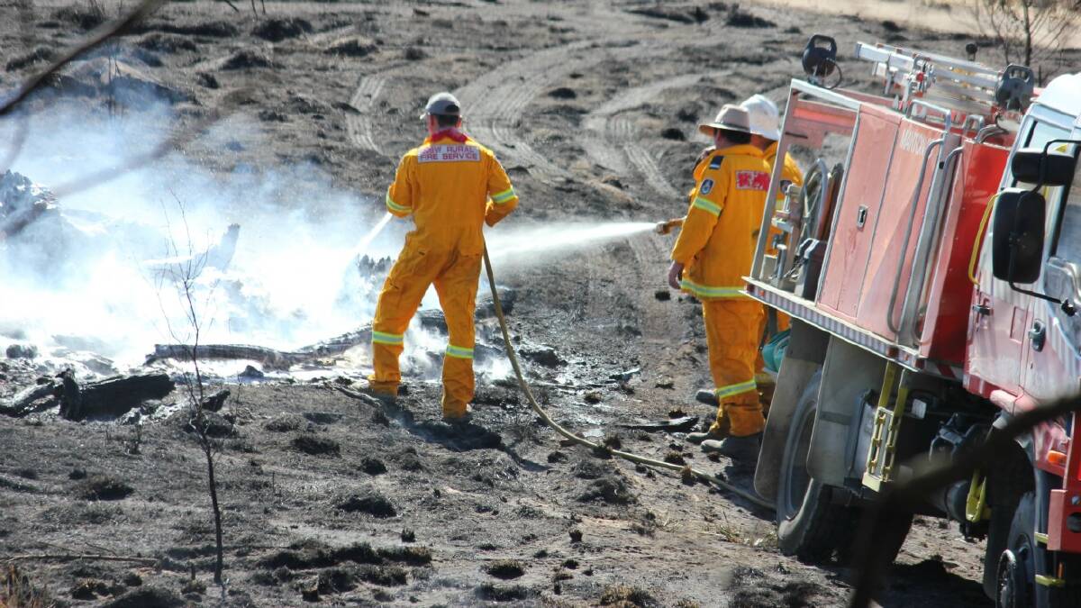ON SCENE: A Rural Fire Service crew battled a fire southwest of Gunning on Monday which burnt out more than 76 hectares and injured a fire fighter when the blaze overtook a truck. Inset: The fire burning freely beside a road. Photos: Chris Gordon